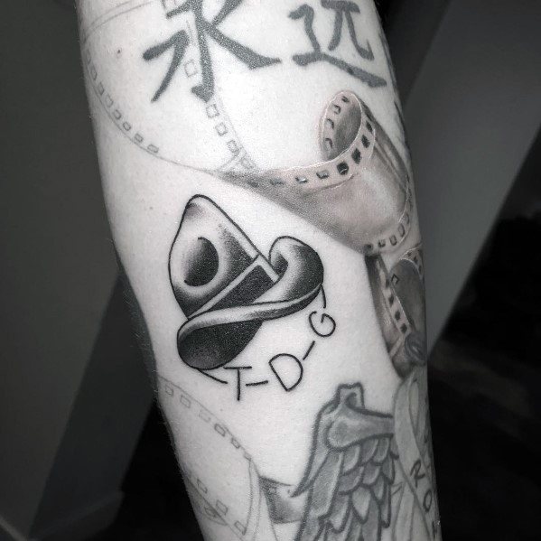 Black and gray tattoo of a cowboy hat with the letters "T-D-G" beneath it, done in a minimalist style with smooth shading and clean linework.
