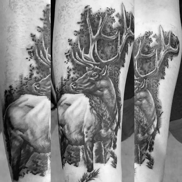 Realistic black and grey elk tattoo on the forearm, featuring intricate shading, bold antlers, and a detailed forest background for a striking design.