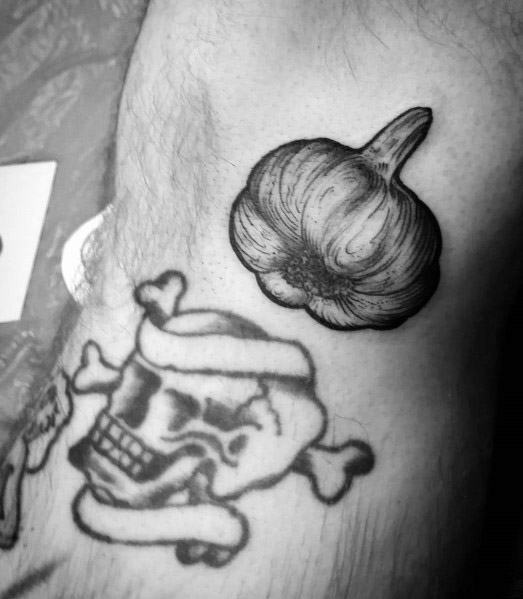 Black and grey garlic tattoo with fine shading and bold details, placed alongside a skull design for a unique and edgy contrast.