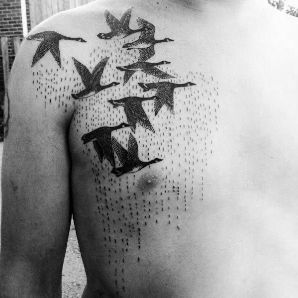 Black and gray tattoo of a flock of geese in flight, inked across the chest and shoulder with fine dot shading to create a rain effect.