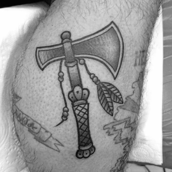 Black and grey tomahawk tattoo with a double-edged blade, intricate handle details, and decorative feathers, designed in a traditional style.