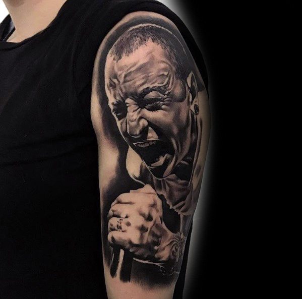 Black and gray tattoo of Chester Bennington mid-performance, capturing his intense emotion with lifelike shading on the upper arm.