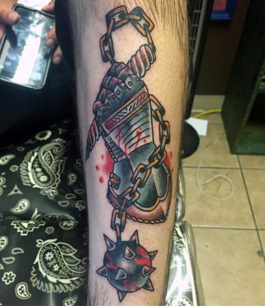 Colorful mace tattoo featuring an armored hand gripping a chain with a spiked ball, accented by red shading and blood drops, symbolizing strength and battle.