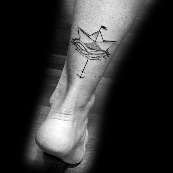 Minimalist black ink tattoo of a paper boat with a small flag, floating on waves, connected to an anchor below, symbolizing adventure and stability.
