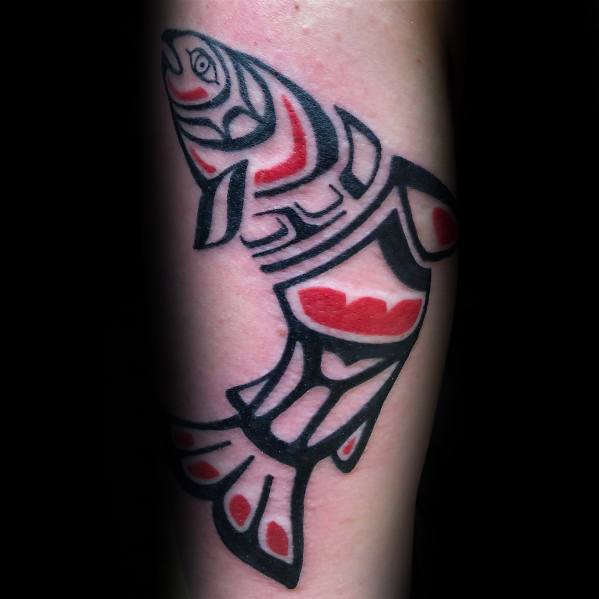Bold tribal-style salmon tattoo in black and red, inspired by Indigenous art, featuring intricate patterns for a striking and symbolic forearm design.