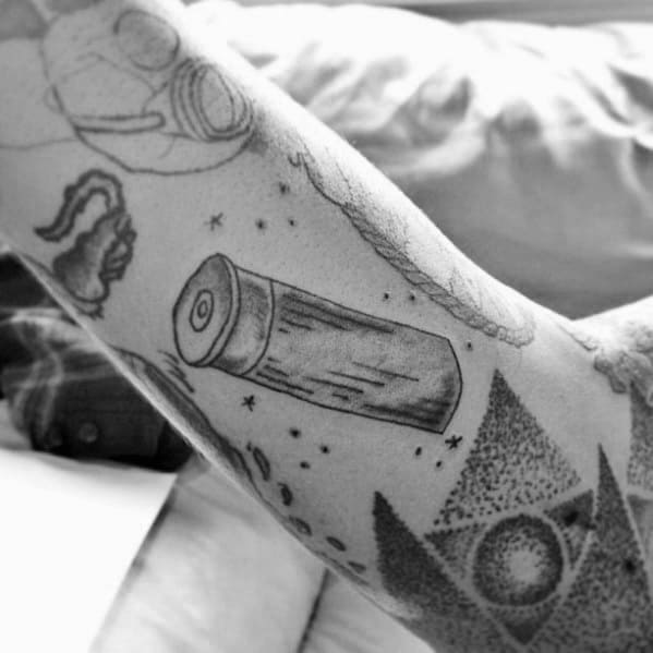 Minimalist black and grey shotgun shell tattoo on the arm, featuring fine linework and subtle shading for a simple yet detailed design.