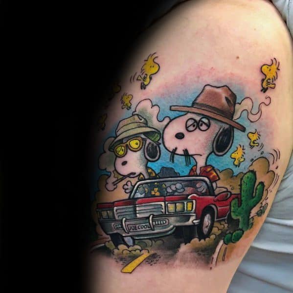 Colorful tattoo of Snoopy and Woodstock dressed as travelers in a red convertible, surrounded by cacti and swirling dust on an arm.