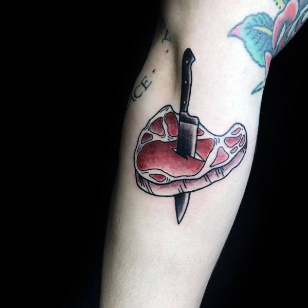 Tattoo of a steak pierced by a knife, featuring bold black outlines and red shading, creating a striking and edgy meat-inspired design.