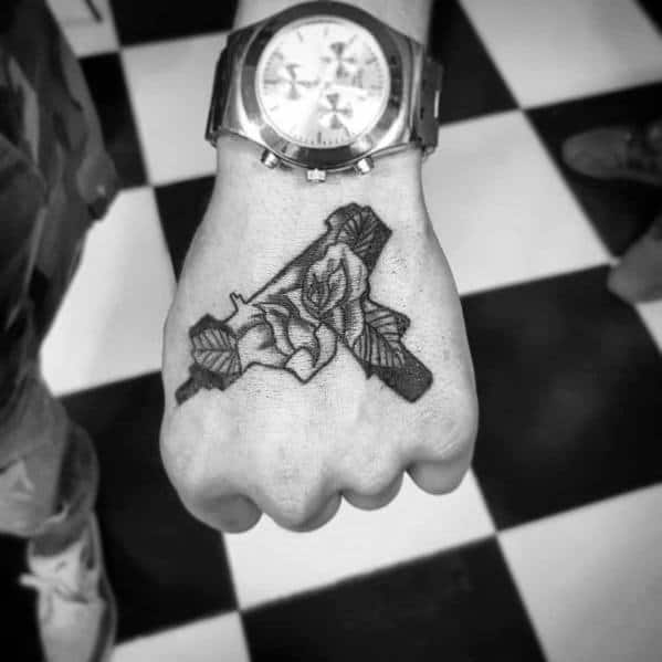Black and grey Uzi tattoo on the hand with a detailed rose integrated into the design, blending bold firearm imagery with floral elegance.