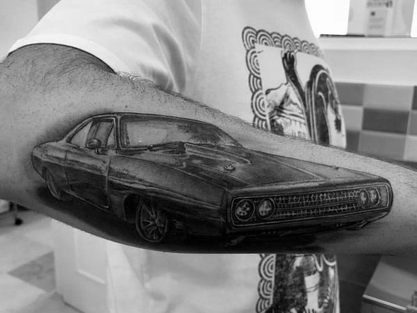 Realistic black and grey Dodge muscle car tattoo on forearm, featuring detailed shading and a bold front grille for a classic look.