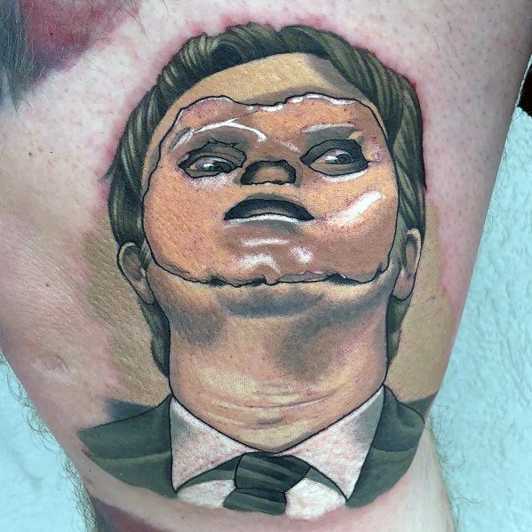 Realistic tattoo of Dwight Schrute with a puppet-like face, featuring detailed shading and bold colors, capturing his intense expression on a leg.