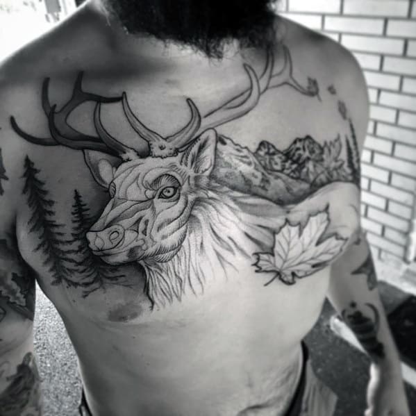 Black and grey elk tattoo on the chest, featuring detailed antlers, a mountain landscape, trees, and a maple leaf for a bold nature-inspired design.