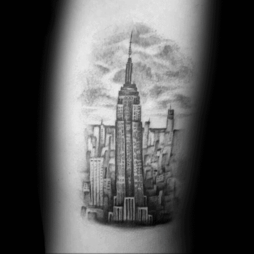 Empire State Building tattoo with a softly shaded New York City skyline and cloudy sky background, inked realistically in black.