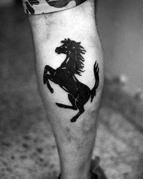 Solid black Ferrari prancing horse tattoo on man's calf, representing strength, speed, and timeless automotive passion.