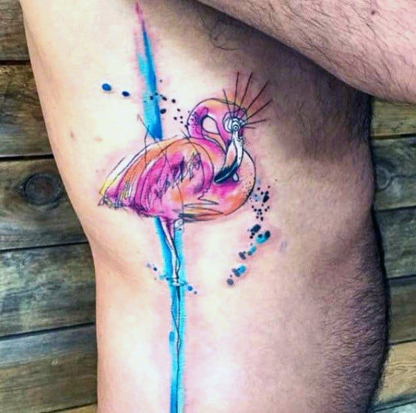 Watercolor flamingo tattoo with bright pink and blue splashes, expressive brushstroke details, and a vibrant artistic design on the ribcage.