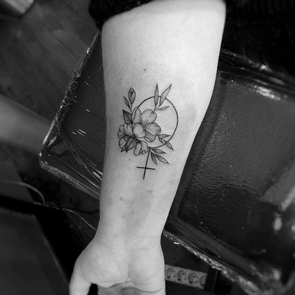 Delicate black ink tattoo of the Venus symbol adorned with blooming flowers and leaves, representing femininity and nature