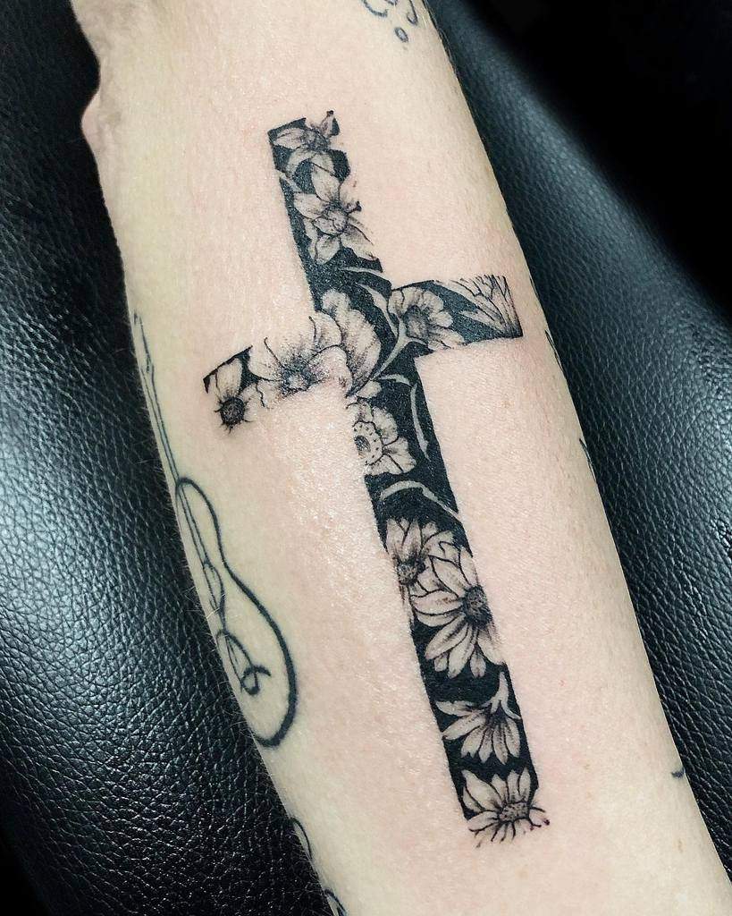 Black ink tattoo of a cross filled with intricate floral patterns, featuring delicate flowers and leaves for a bold yet elegant design