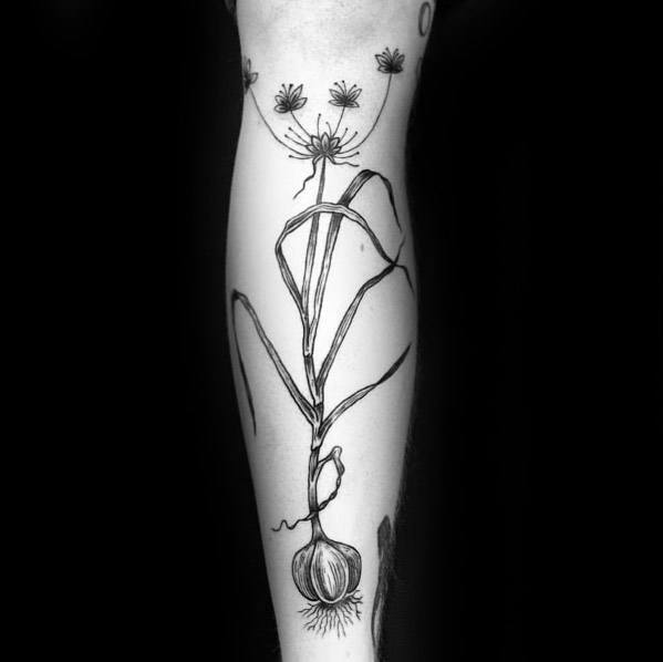 Delicate black and grey garlic plant tattoo with fine linework and botanical details, creating an elegant and organic design on the forearm.