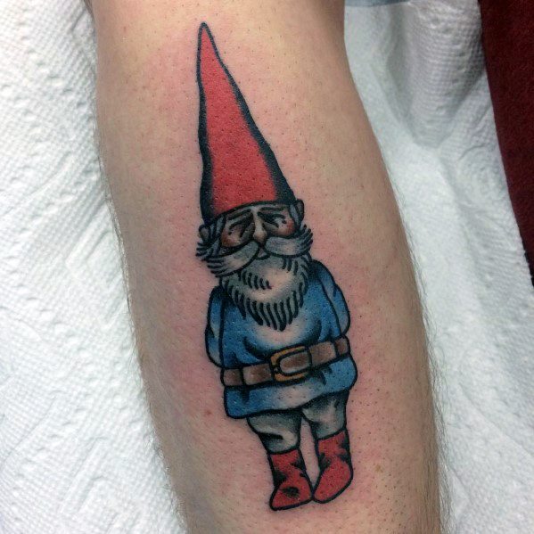 Tattoo of a sleepy-looking gnome with a tall red hat, blue coat, and red boots, standing with a relaxed posture and a peaceful expression.