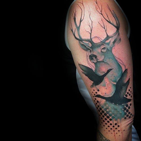 Watercolor-style tattoo of a majestic deer with detailed antlers, accompanied by flying geese and abstract dot work, inked on the upper arm.