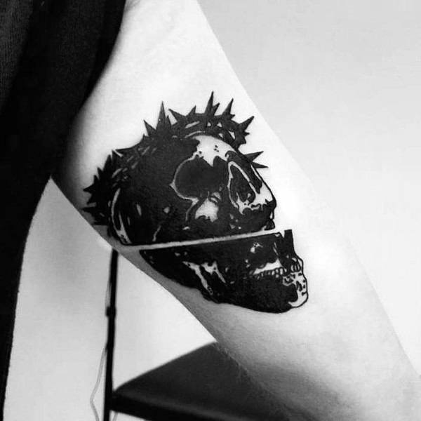 Bold blackwork tattoo featuring a split skull with a crown of thorns, creating a striking gothic and surreal design on the arm.