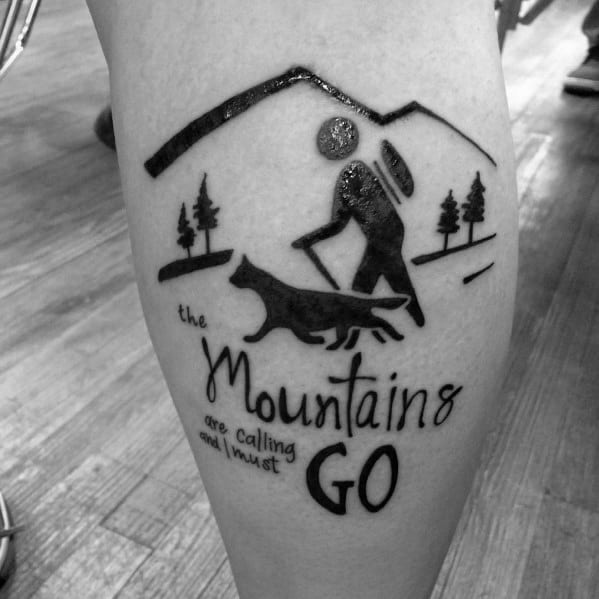 Minimalist hiking tattoo with a hiker, dog, mountains, and the quote 'The mountains are calling and I must go,' symbolizing adventure.