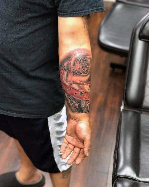 Realistic Honda engine tattoo on a man's forearm, featuring a detailed mechanical design with bold red and metallic shading for a dynamic effect.