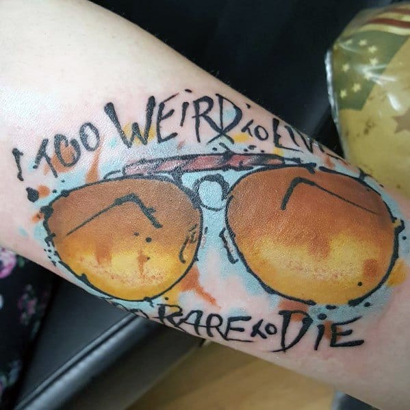 Watercolor-style Hunter S. Thompson tattoo featuring aviator glasses with a desert reflection and the quote "Too Weird to Live, Too Rare to Die" in bold lettering.