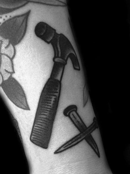 Bold blackwork tattoo of a hammer and crossed nails, symbolizing strength, craftsmanship, and dedication to woodworking and construction.