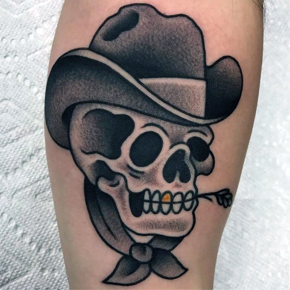 Black and gray tattoo of a cowboy skull wearing a hat and bandana, biting down on an arrow, done in a bold traditional Western style.