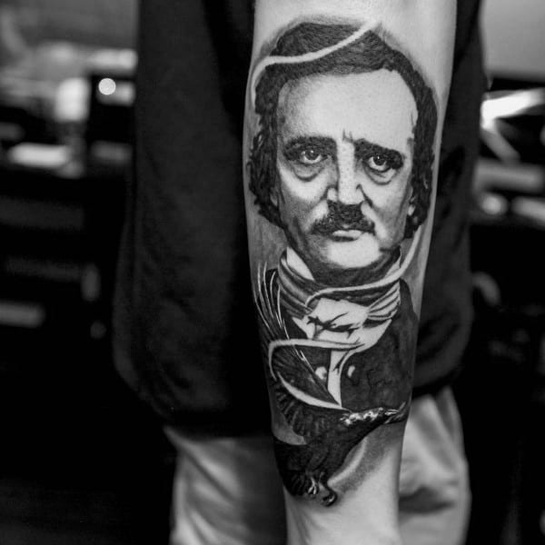 Black and grey forearm tattoo of Edgar Allan Poe with a solemn expression, featuring a detailed raven and flowing ribbon beneath his portrait.