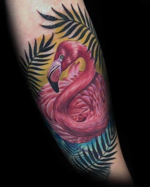 Realistic flamingo tattoo with vibrant pink feathers, surrounded by tropical palm leaves and a warm gradient background for a bold, exotic look.