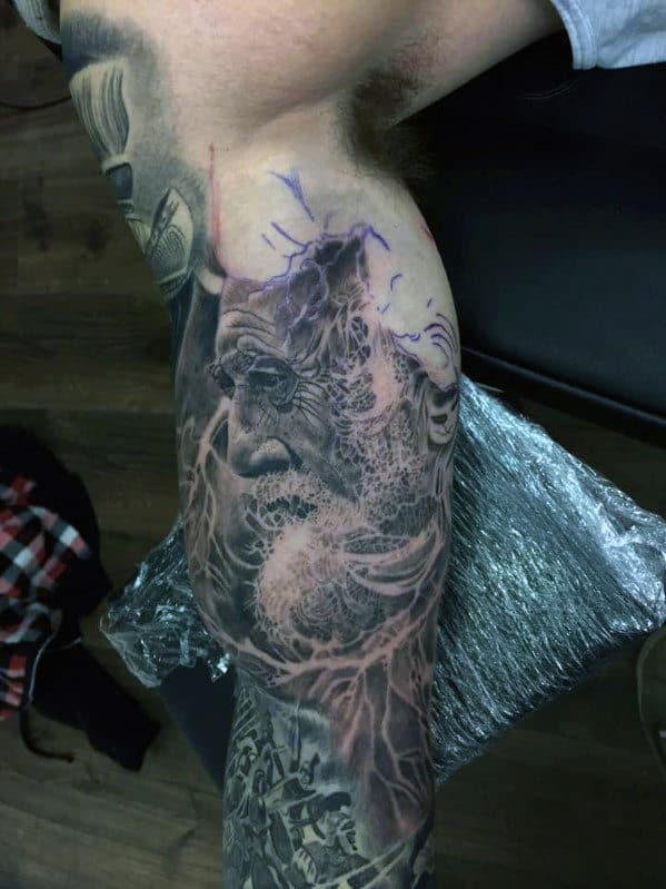 Arm tattoo featuring a detailed portrait of a bearded man with other intricate designs