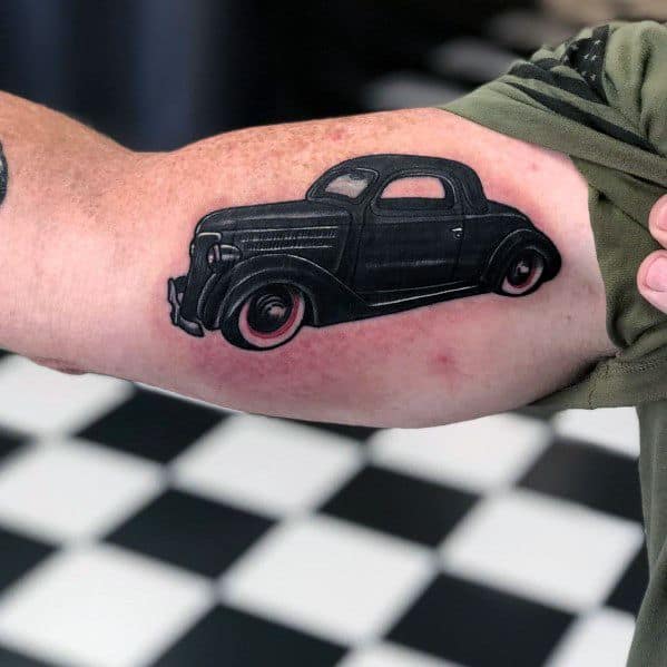 Bold black vintage Ford coupe tattoo on forearm, featuring a classic hot rod design with clean lines and subtle red shading on the wheels.