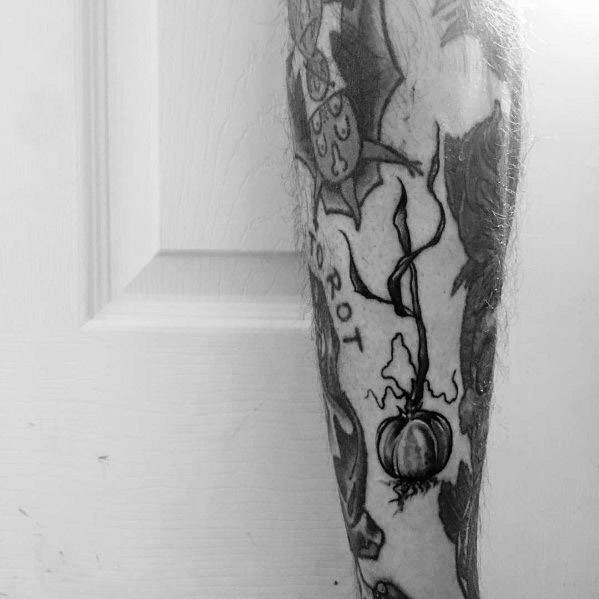 Black and grey garlic tattoo with fine linework and delicate root details, blending seamlessly with other tattoos for a bold botanical design.