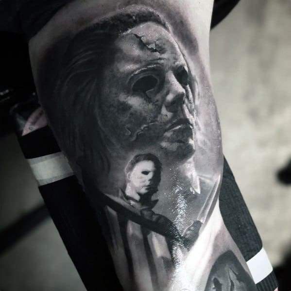 Hyper-realistic black and grey Michael Myers tattoo featuring his worn mask and a shadowy figure holding a knife for a chilling effect.
