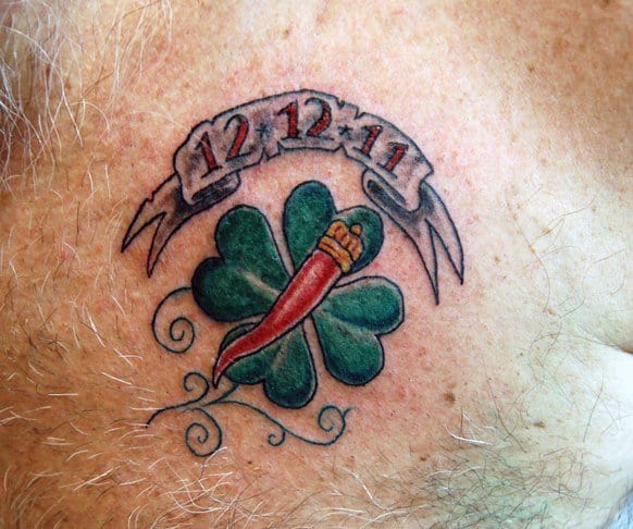 Italian horn tattoo with a crowned design over a four-leaf clover and a banner with '12-12-11,' symbolizing luck and a meaningful date.