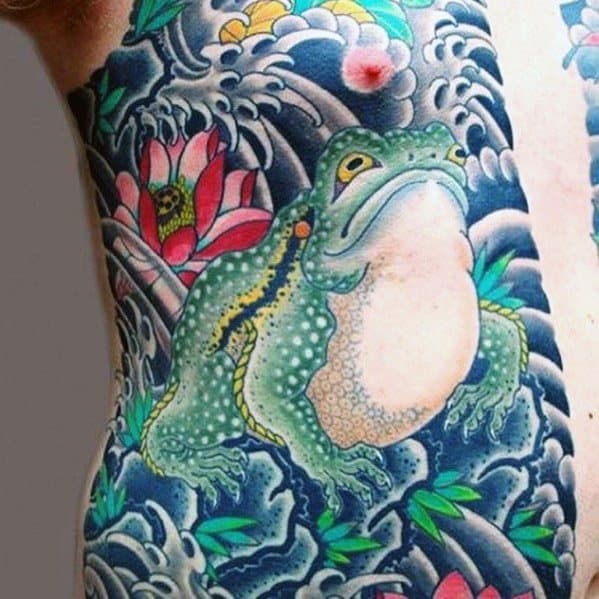 Japanese-style tattoo featuring a large green frog surrounded by swirling waves, lotus flowers, and lush foliage, symbolizing nature, strength, and transformation.
