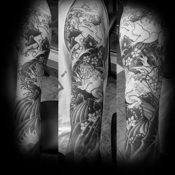 Black and grey Japanese-style full-sleeve tattoo featuring dynamic frogs amidst swirling waves, cherry blossoms, and intricate traditional patterns.