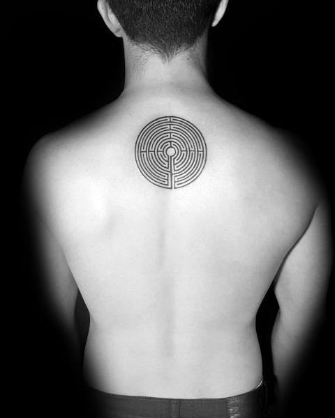Minimalist circular labyrinth tattoo on a man's upper back, featuring a clean geometric maze design with a single path leading to the center.