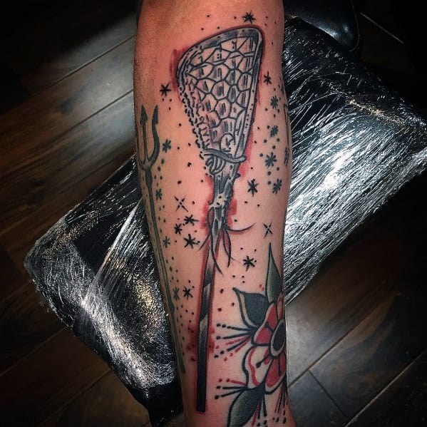 Traditional-style lacrosse stick tattoo with bold black outlines, red shading, and decorative stars, placed on the forearm for a striking look.