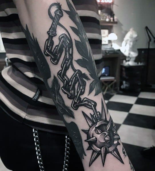 Black and gray mace tattoo featuring a spiked ball on a heavy chain wrapping around the forearm, symbolizing strength, resilience, and battle.