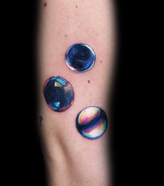 Realistic tattoo of three glossy marbles with vibrant reflections and deep shading, creating a striking 3D effect on the forearm.