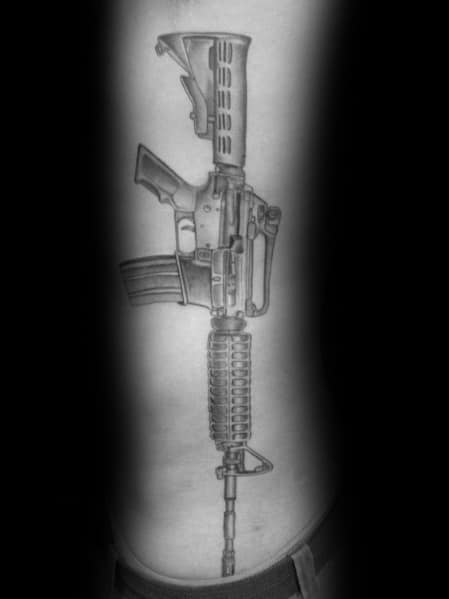 Large black and grey AR-15 tattoo on the ribcage, featuring detailed shading and realistic design, symbolizing strength, resilience, and firearm appreciation.
