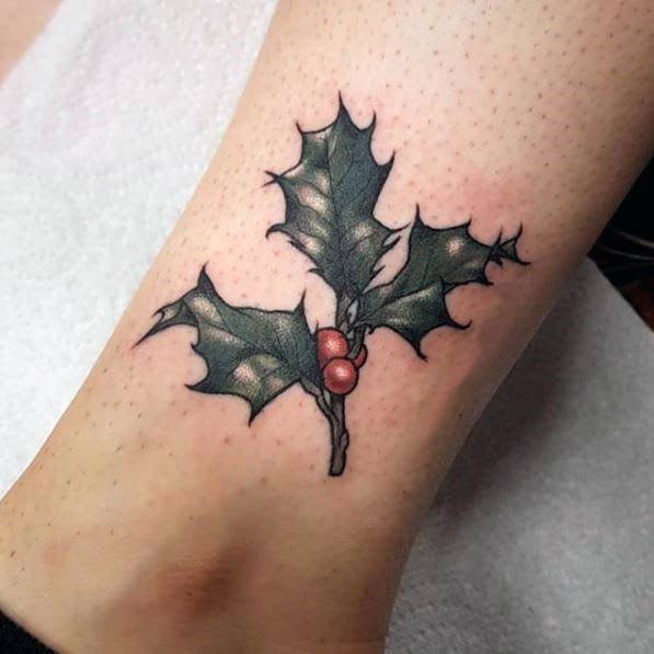 Christmas tattoo of a simple and elegant holly sprig with dark green leaves and red berries, designed with fine shading for a classic festive look.