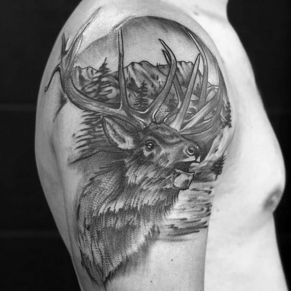 Realistic black and grey elk tattoo on the upper arm, featuring intricate shading, bold antlers, and a detailed mountain landscape for a striking design.
