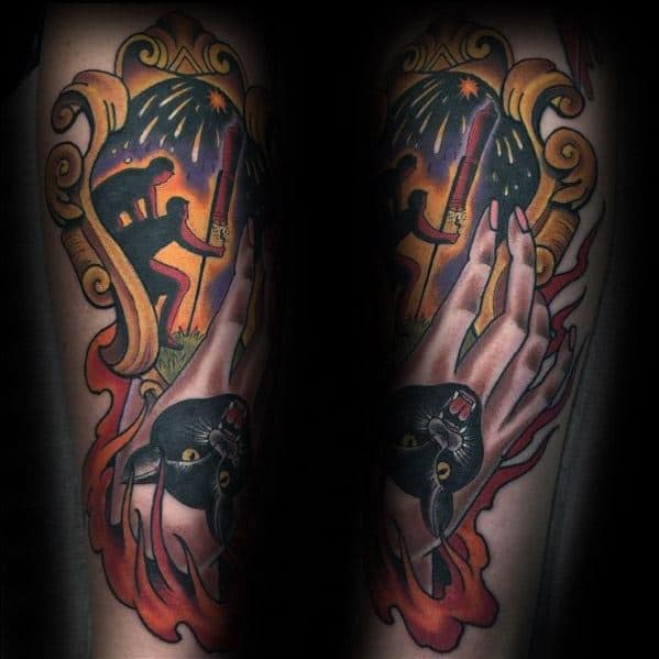 Tattoo featuring a dramatic scene with a silhouetted figure lighting a firework, a black panther head, and fiery elements, framed by ornate golden details.
