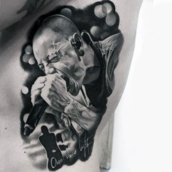 Realistic black and gray tattoo of Chester Bennington passionately singing, with 'One More Light' and a silhouette tribute at the bottom.