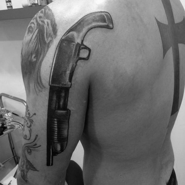 Realistic black and grey shotgun tattoo on the upper arm, featuring bold shading and fine details for a striking and powerful design.
