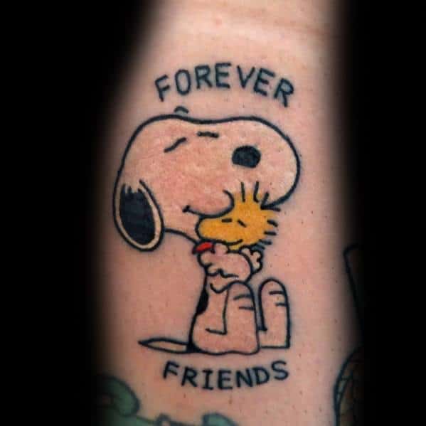 Colorful tattoo of Snoopy hugging Woodstock with the words "FOREVER FRIENDS" above and below, placed on a person's arm.